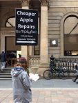 A person holding a golf sale type sign that says, Cheaper Apple repairs at SimplyFixIt