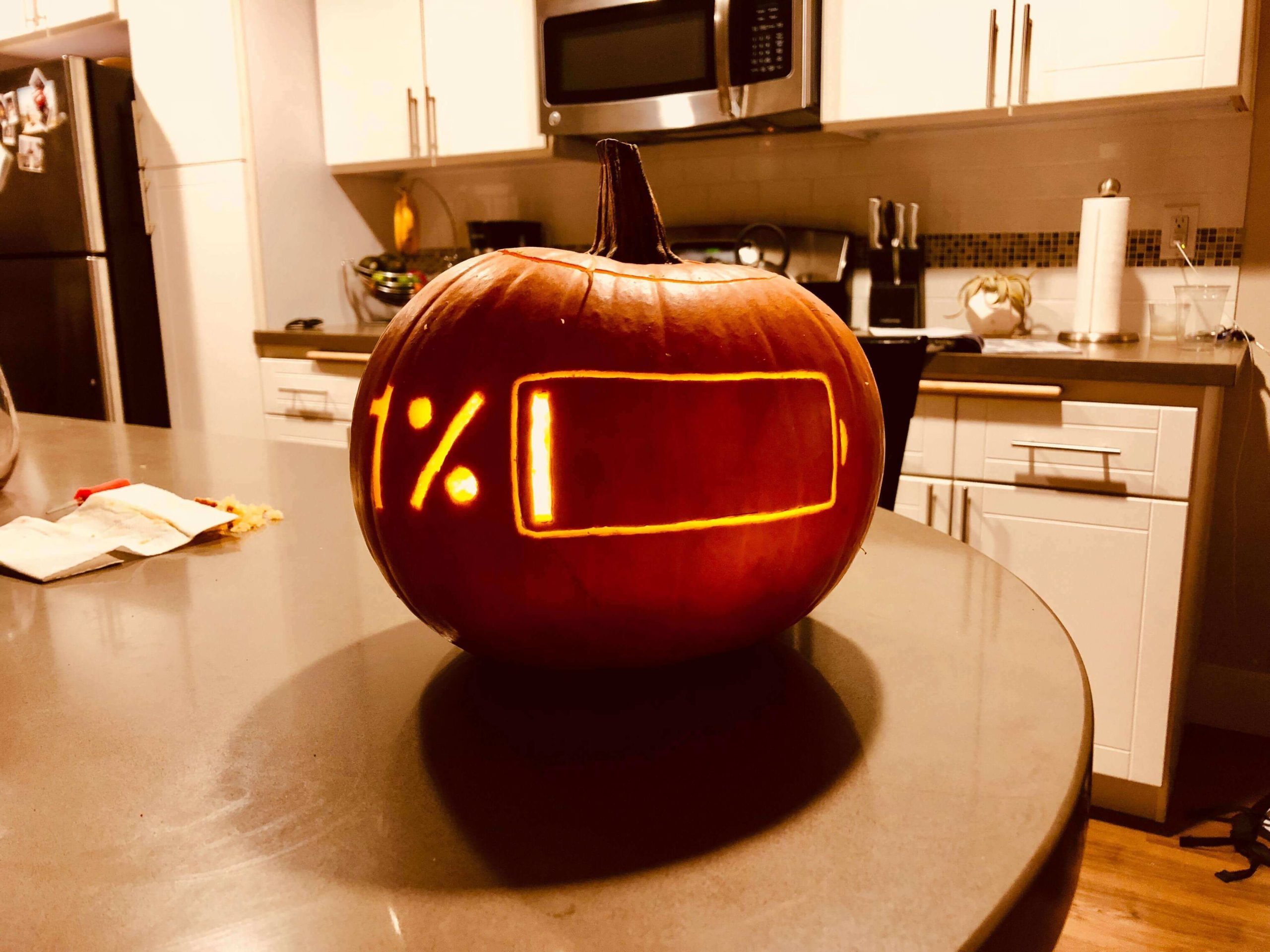 A pumpkin carved for halloween. It has the shape of a battery on it, with the 1% showing.
